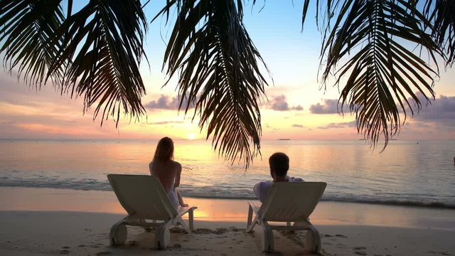 Couple on a tropical beach are admiring the sunset.