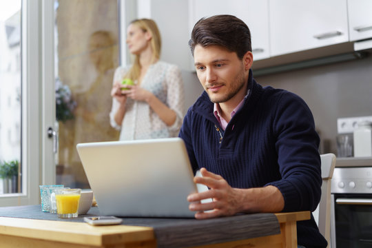 mann sitzt in der küche und schaut konzentriert auf seinen laptop