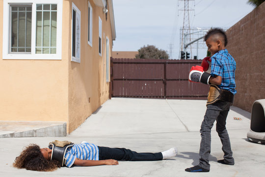 Two boys in yard, one wearing boxing gloves the other lying on back