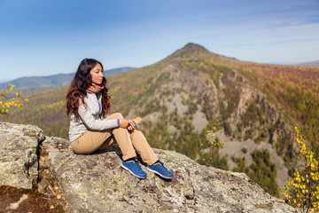 Young woman hiker sitting on cliff's edge and looking to a blue