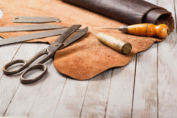Leathersmith's work desk . Pieces of hide and leather working tools on a work table. - obrazy, fototapety, plakaty