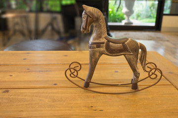 Craving wooden horse toy / Craving wooden horse toy on wooden table in evening with garden view from window 