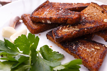 Roasted salted garlic croutons with fresh parsley and piese of  garlic on white plate.