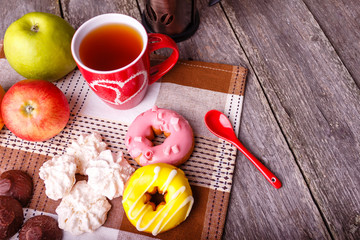 Donut and different sweet food and a cup of tee. Rustic wooden table. Bakery, sweet doughnut, coconut cakes and fresh fruits on breakfast.