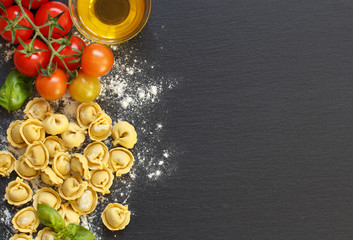 Fresh tortellini pasta and ingredients on a dark board