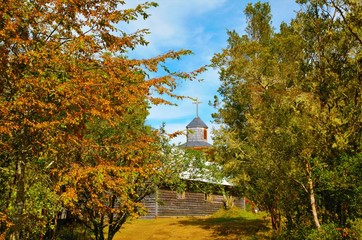Fototapeta premium View through trees onto the old wooden church on the small island Aucar close to Quemchi on the island Chiloé in Chile