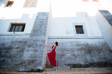 Fashion style portrait of young beautiful calm female model posing at city street with magnificent architecture. Full body portrait.