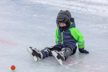 Fototapeta na wymiar Little boy in skates sitting on ice