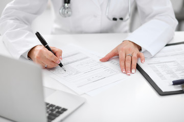 Close-up of a female doctor filling  out application form , sitting at the table in the hospital