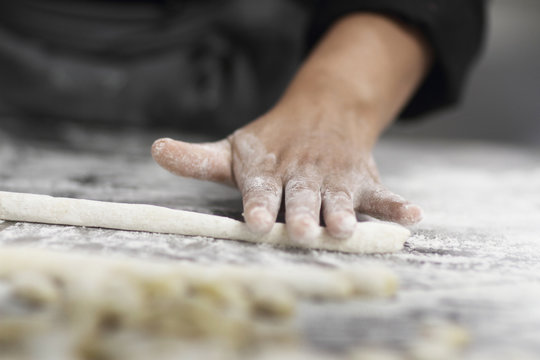 Woman working in restaurant kitchen, cropped hand rolling pastry
