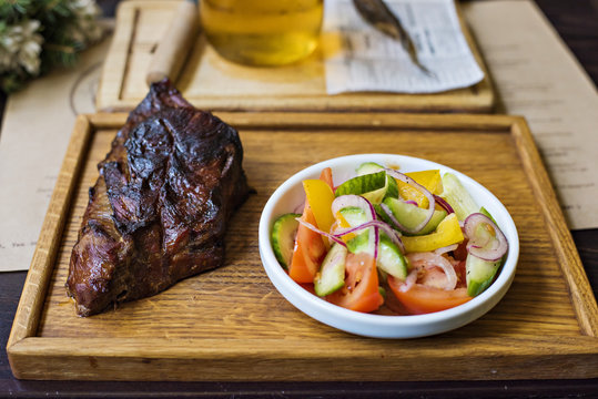 On a wooden tray grilled meat and a salad of cucumber and tomato