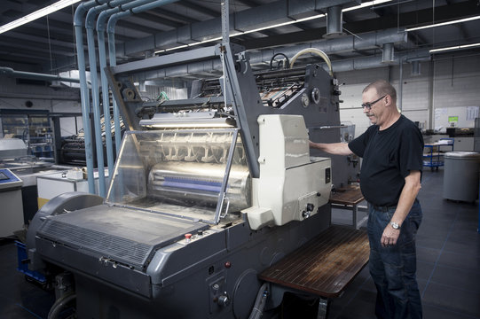 Worker operating print machine in printing workshop