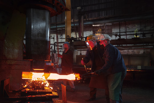Forge workers pre form red hot steel billet into flight bar (mining component) on hammer