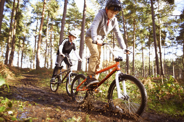 Twin brothers racing BMX bikes through muddy forest
