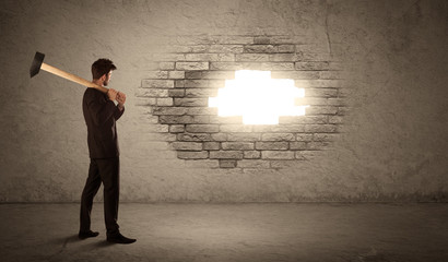 Business man hitting brick wall with hammer and opening a hole