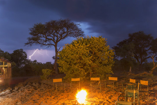 Campfire and a row of empty chairs at night, Kasane, Chobe National Park, Botswana, Africa