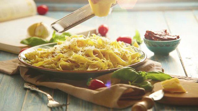 A cook grates the cheese upon the plate of Italian pasta