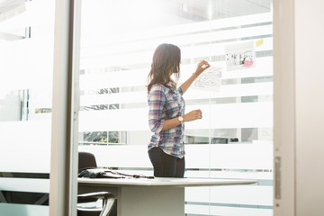 Young businesswoman putting post it notes on office window