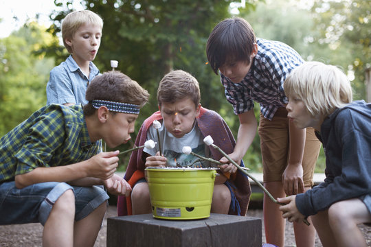 Group of young boys toasting marshmallows over bucket barbecue