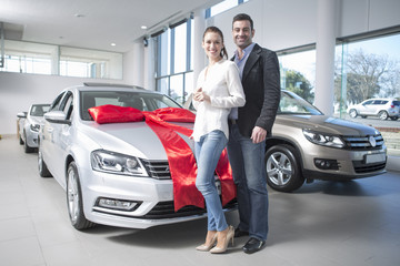 Portrait of mid adult couple and new car with red bow in car dealership