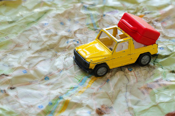 Mini car and a red plastic suitcase on a map. Closeup