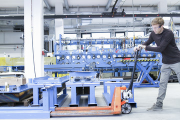 Mid adult male moving products on pallet jack in engineering plant