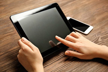 Mobile phone and female hands using tablet, on the wooden background