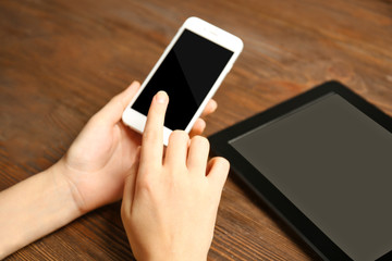 A tablet and female hands using mobile phone, on the wooden background