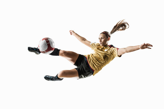 Studio shot of young female soccer player kicking ball mid air