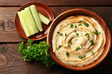 Tuinposter Wooden bowl of tasty hummus with parsley and cucumber on table, close up © Africa Studio