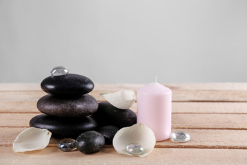 Fototapeta na wymiar Spa stones with white petals and pink candle on wooden table against grey background