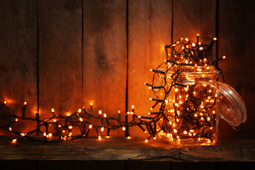 Glass jar with lighted garland on wooden background