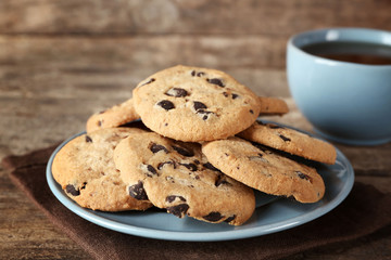 Chocolate chip cookies on a blue plate and a cup of tea on wooden table