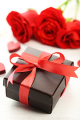 Gift box, rose flowers and decorative hearts on light wooden background