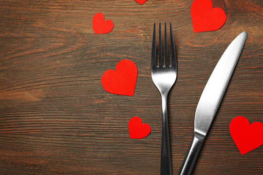 Fork and knife with decorative paper hearts, on wooden background