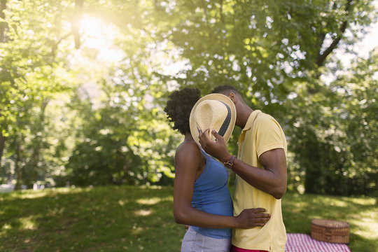 Young couple in park holding up hat to cover faces