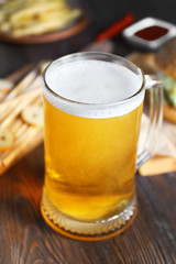 Glass mug of light beer with snacks on dark wooden table, close up