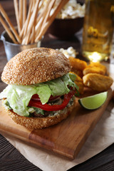 Big tasty hamburger with snacks and glass bottle of light beer on wooden table
