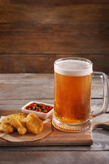 Glass mug of light beer with snacks on wooden table, close up