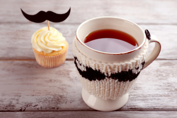 Delicious creative cupcake with mustache and cup of tea on wooden table
