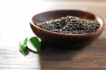 Granulated tea with green leaves in wooden bowl on table closeup