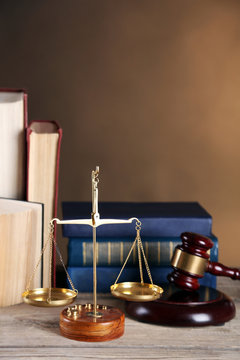 Wooden gavel with justice scales and books on brown background