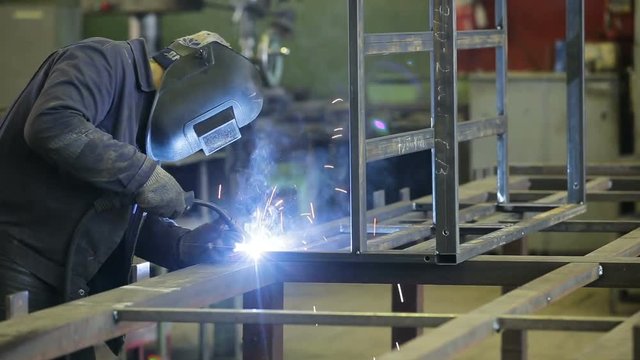 Welder working a welding metal with protective mask and sparks.Metal worker welds two pieces of metal together.Man in welding mask makes welding metal products factory