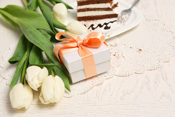 Sweet creamy cake with flowers and present box on wooden table closeup