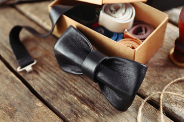 Black bow tie and full cardboard gift box of ties on wooden table, close up