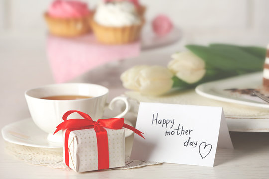 Happy mother day greeting with tulips, cup of tea and present box on wooden table closeup