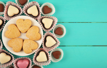 Valentine's Day concept. Composition of delicious chocolate candies and tasty cookies on turquoise wooden background