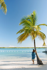 Obraz premium Young woman leaning against palm tree, Providenciales, Turks and Caicos Islands, Caribbean
