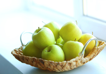 Ripe green apples in a wicker basket on windowsill