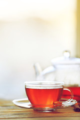 Glass cup of tea with teapot on wooden table against blurred background
